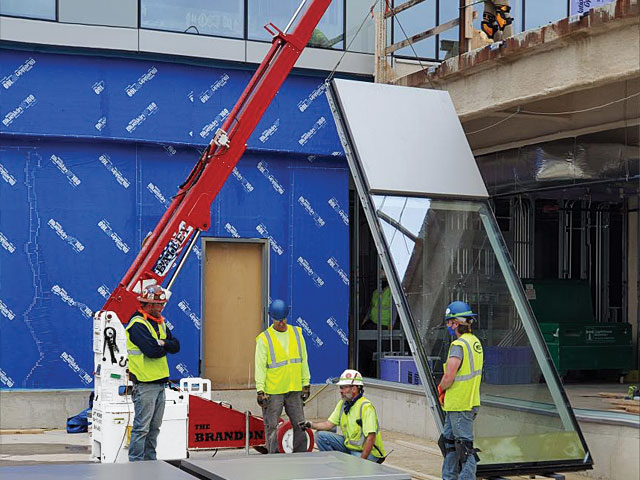 The Brandon crane at a commercial construction site lifting a large structural glass panel with crew