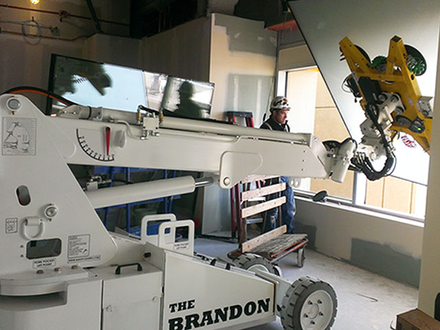 The Brandon Compact handler holding a large glass panel in a fabrication facility