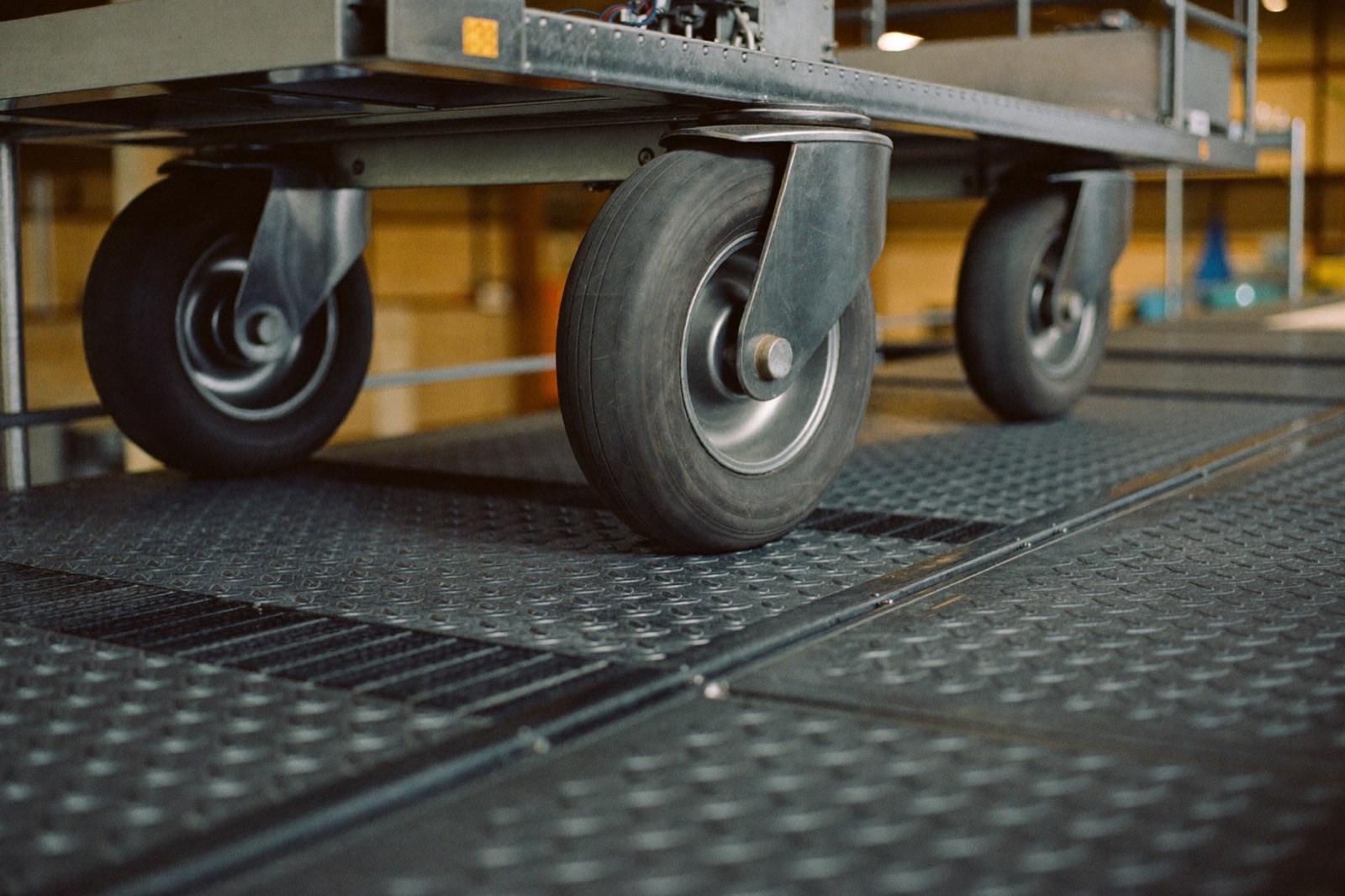 Cart wheels rolling up a diamond-plate ramp onto a drive-on scissor lift platform deck
