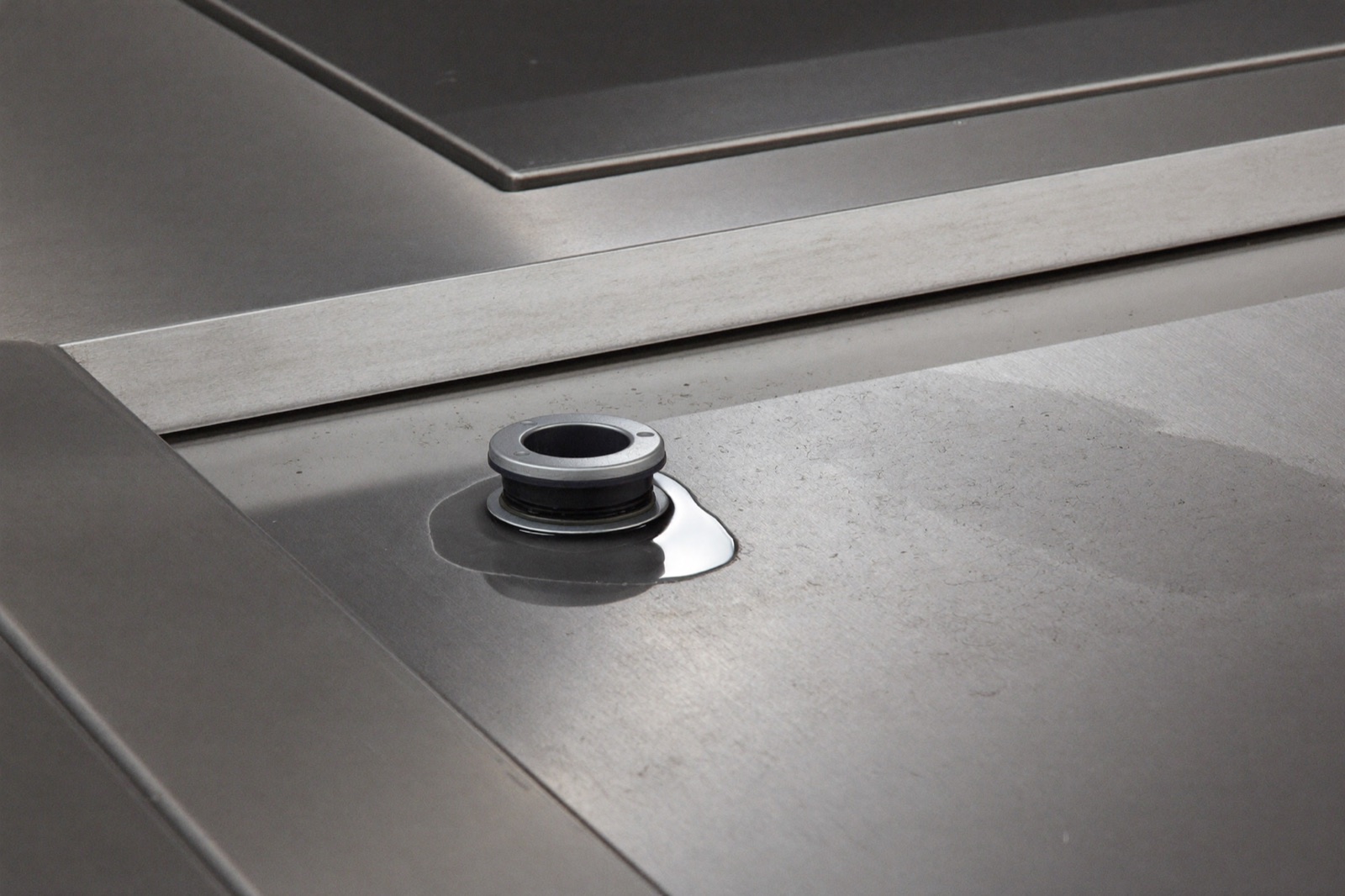 Recessed steel containment tray with raised coaming lip and capped drain fitting on an industrial lift deck