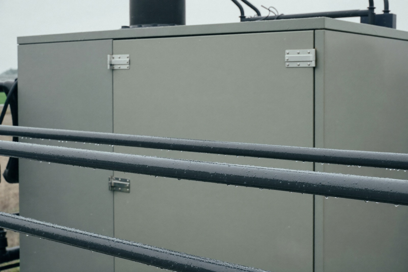 Rain beading on a powder-coated handrail beside a sealed weatherproof industrial control enclosure